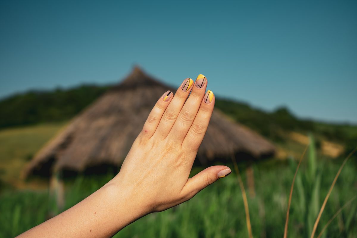 A close-up of a hand showcasing stylish nail art set against a rustic countryside background.